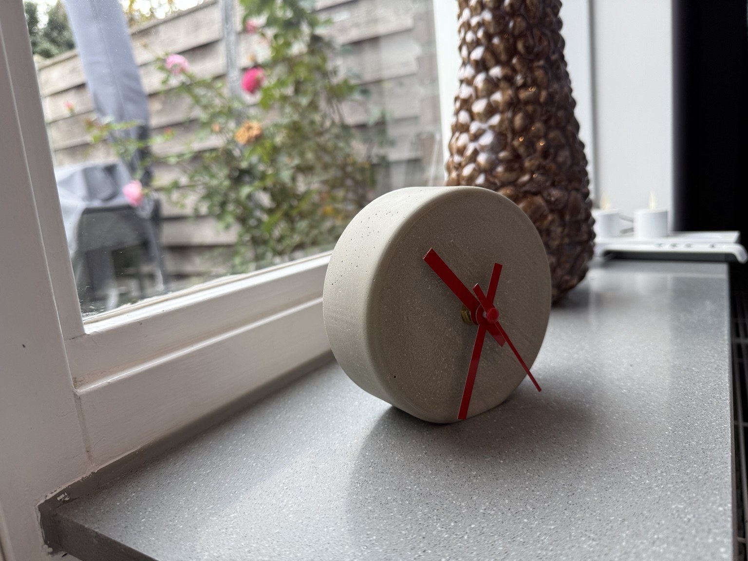 Rond betonklokje met rode wijzers op een vensterbank
