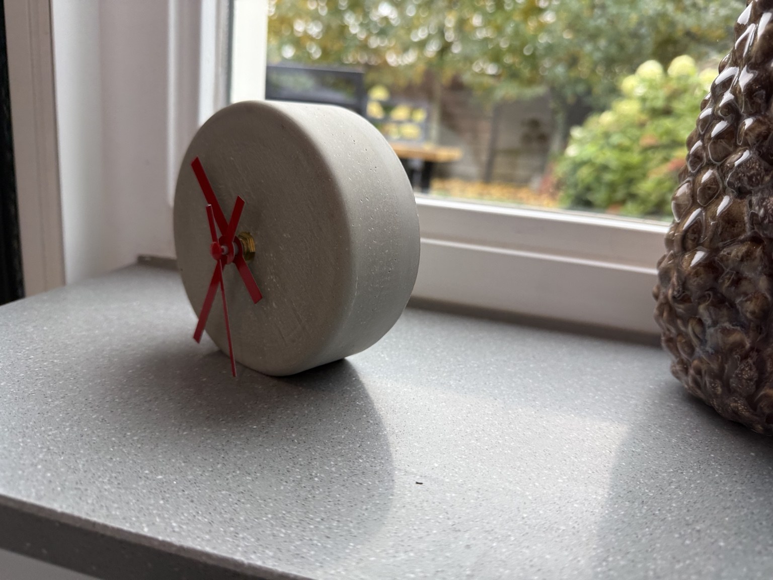 Detail van het ronde betonklokje met rode wijzers